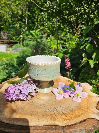 Eine dekorative Etagere auf einem Holzscheit, umgeben von lila und rosa Blumen.