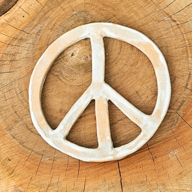 Ein Keramikanhänger in Form eines Peace-Zeichens auf einem Holzuntergrund.