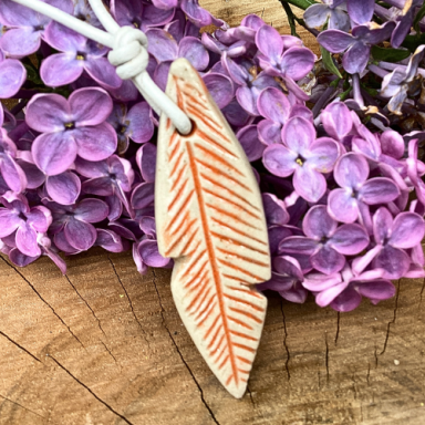 Hängende Kette mit einem gefiederten Anhänger in der Mitte von lila Fliederblüten.