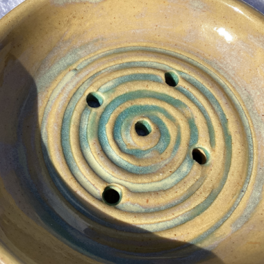Keramikschale mit spiralförmigen Reliefs und fünf Löchern in der Mitte.