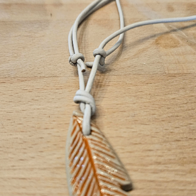 Halskette mit einem orangefarbenen, federförmigen Anhänger und einem hellen Band.