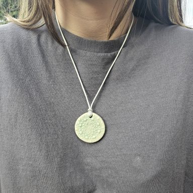 Person trägt eine silberne Kette mit einer runden, grünen Medaille.