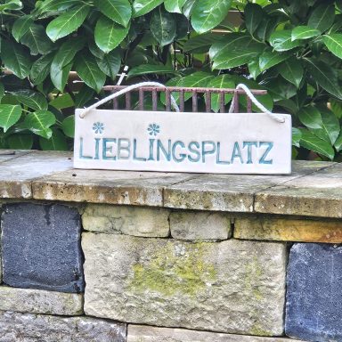 Schild mit der Aufschrift "Lieblingsplatz" vor einer grünen Hecke.
