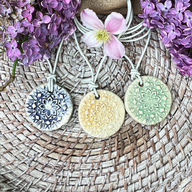 Drei Rundanhänger in Blau, Gelb und Grün auf einer geflochtenen Unterlage mit Blumen.