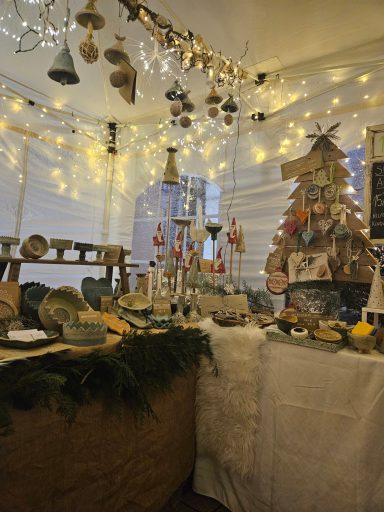 Festlich dekorierter Marktstand mit Beleuchtung, Weihnachtsbaum und handgefertigten Waren.
