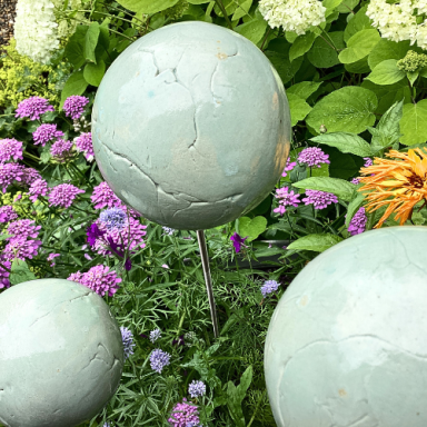 Drei grüne Kugeln stehen zwischen bunten Blumen im Garten.