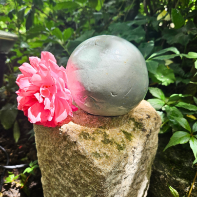 Türkise Rosenkugel auf einem Stein, daneben eine pinke Blume.
