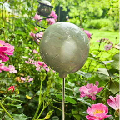 Kugel aus Keramik auf einem Stab, umgeben von bunten Blumen im Garten.