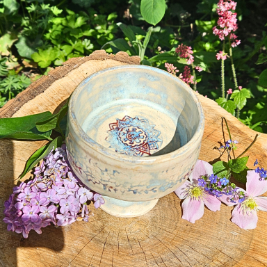 Schüssel aus Keramik, umgeben von Blumen auf einem Holzstamm.