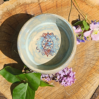 Schüssel mit blauem Muster, umgeben von Blumen auf einer Holzoberfläche.