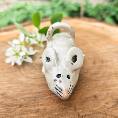 Beige Keramik Maus mit Blumen und Holzuntergrund.