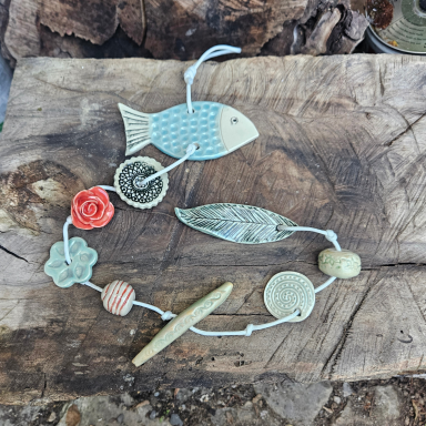 Kette aus Anhängern in Form von Fischen, Blumen und Kugeln auf Holzuntergrund.
