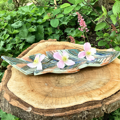 Bunte Schale aus Keramik mit rosa Blumen auf einem Baumstamm im Grünen.