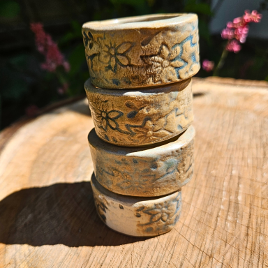 Vier dekorative Ringe mit floralen Mustern auf einem Holzuntergrund.