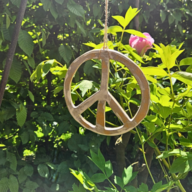 Hängendes Peace-Zeichen vor grünen Pflanzen und einer rosa Blüte.